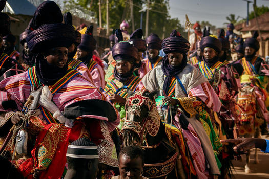 Zaria city Nigeria 21 March 2026 View of a vibrant procession of men in richly embroidered flowing robes and deep indigo turbans riding ornately decorated horses under the bright sun. Zaria city Nigeria 21 March 2026 View of a vibrant procession of men in richly embroidered flowing robes and deep indigo turbans riding ornately decorated horses under the bright sun.