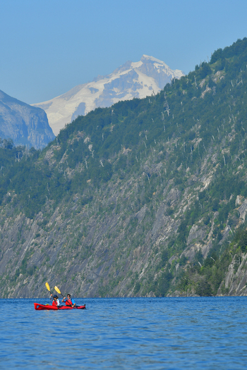 View of people in a red kayak on the blue waters of Nahuel Huapi Lake with steep forested mountains and a snow capped peak San Carlos de Bariloche Rio Negro Argentina. View of people in a red kayak on the blue waters of Nahuel Huapi Lake with steep forested mountains and a snow capped peak San Carlos de Bariloche Rio Negro Argentina.