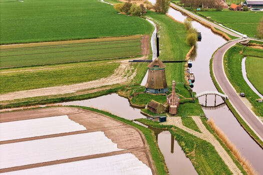 Aerial view of De Kaagmolen windmill beside a winding canal and vibrant green agricultural fields in Spanbroek North Holland Netherlands. Aerial view of De Kaagmolen windmill beside a winding canal and vibrant green agricultural fields in Spanbroek North Holland Netherlands.