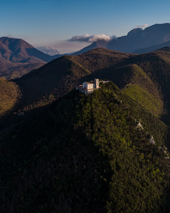 Aerial view of Santuario del Santissimo Salvatore perched on a mountain peak surrounded by forested hills and distant peaks in Montella Campania Italy. Aerial view of Santuario del Santissimo Salvatore perched on a mountain peak surrounded by forested hills and distant peaks in Montella Campania Italy.