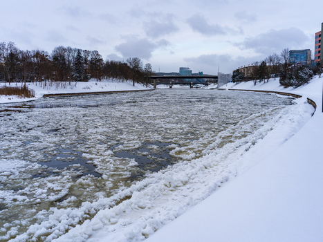 View of the ice covered Neris River flowing through the city with snow covered banks and a bridge in the distance under a cloudy winter sky in Vilnius Vilnius County Lithuania. View of the ice covered Neris River flowing through the city with snow covered banks and a bridge in the distance under a cloudy winter sky in Vilnius Vilnius County Lithuania.