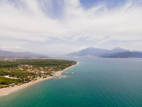 Aerial view of Karaot Beach with turquoise waters sandy shoreline lush vegetation and a small pier set against distant mountains under a bright sky in Fethiye Mugla Turkiye. Aerial view of Karaot Beach with turquoise waters sandy shoreline lush vegetation and a small pier set against distant mountains under a bright sky in Fethiye Mugla Turkiye.