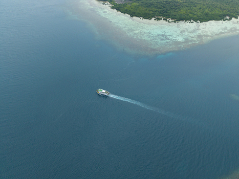 Aerial view of a ferry sailing on the deep blue sea near the shore where the lush green island contrasts with the turquoise waters Karimunjawa Jawa Tengah Indonesia. Aerial view of a ferry sailing on the deep blue sea near the shore where the lush green island contrasts with the turquoise waters Karimunjawa Jawa Tengah Indonesia.