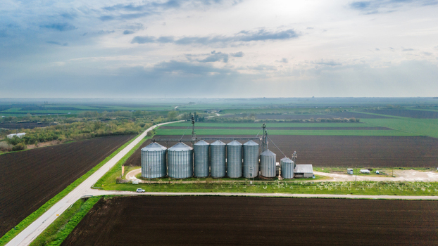 Aerial view of silver grain silos stand as sentinels amidst the patchwork of dark earth and verdant fields under a vast cloud strewn sky Sremska Mitrovica Vojvodina Serbia. Aerial view of silver grain silos stand as sentinels amidst the patchwork of dark earth and verdant fields under a vast cloud strewn sky Sremska Mitrovica Vojvodina Serbia.