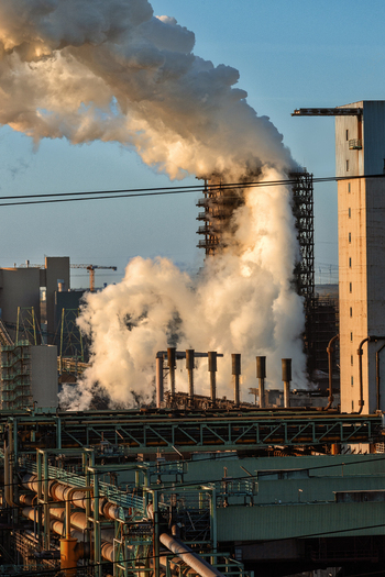 View of thick white smoke rising from industrial chimneys and steel plant structures under a clear sky Duisburg North Rhine Westphalia Germany.