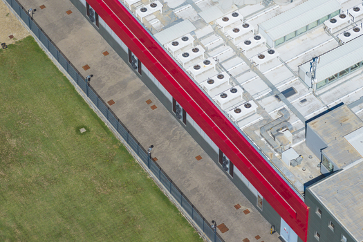 Aerial view of a modern datacenter facility with rooftop cooling units and a red architectural accent situated next to a green lawn in Arezzo Tuscany Italy. Aerial view of a modern datacenter facility with rooftop cooling units and a red architectural accent situated next to a green lawn in Arezzo Tuscany Italy.