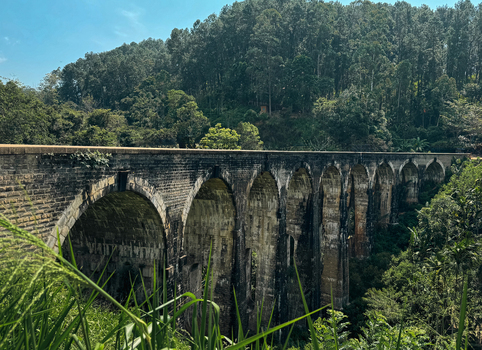 View of the historic Nine Arch Bridge a stone railway viaduct surrounded by lush green forest and dense vegetation in Sri Lanka.