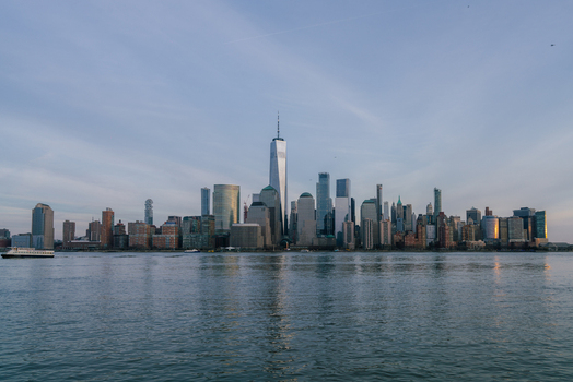 View of the New York City skyline featuring One World Trade Center rising above the skyscrapers along the Hudson River at sunset in New York New York United States.