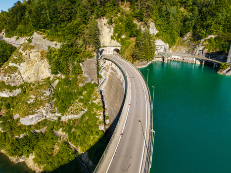 Aerial view of the Barrage de Rossens dam with its curved concrete structure road and turquoise reservoir water by forested cliffs in Pont la Ville Fribourg Switzerland.