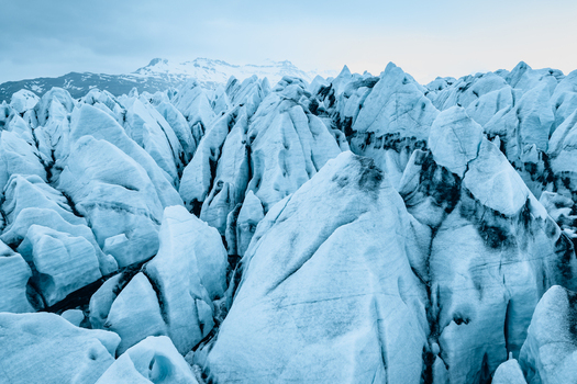 Aerial view of Vatnajokull glacier featuring jagged ice formations deep crevasses and dark volcanic ash streaks under a soft sky in Iceland.