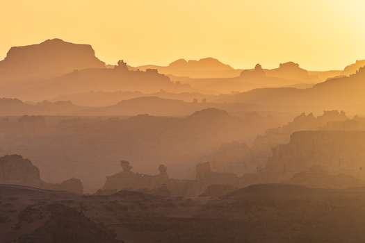 Aerial view of the Tadrart Rouge rock formations and sandstone plateaus under a golden sunset haze in Djanet Illizi Algeria.