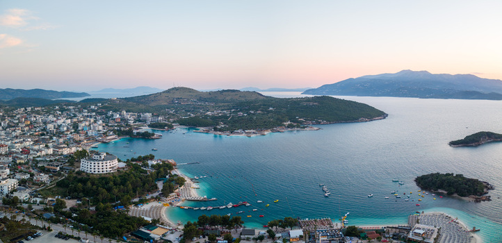 Aerial view of the coastal town of Ksamil featuring turquoise bays sandy beaches with umbrellas and small islands under a soft evening sky Ksamil Vlore County Albania. Aerial view of the coastal town of Ksamil featuring turquoise bays sandy beaches with umbrellas and small islands under a soft evening sky Ksamil Vlore County Albania.