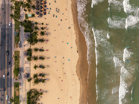 Aerial view of a sandy beach with palm trees beach umbrellas people relaxing on the sand and waves rolling onto the shore next to a coastal road in Vietnam. Aerial view of a sandy beach with palm trees beach umbrellas people relaxing on the sand and waves rolling onto the shore next to a coastal road in Vietnam.