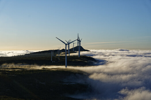 Aerial view of wind turbines at Bica da Cana peak rising above a dense sea of clouds during golden hour in Funchal Madeira Portugal.