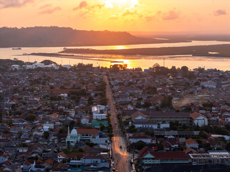 Aerial view of the coastal town of Cilacap at sunset featuring dense residential rooftops a prominent mosque and a main road leading towards the bay in Cilacap Central Java Indonesia. Aerial view of the coastal town of Cilacap at sunset featuring dense residential rooftops a prominent mosque and a main road leading towards the bay in Cilacap Central Java Indonesia.