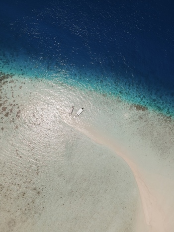 Aerial view of Pasir Timbul Mansuar sandbar surrounded by turquoise shallow water and deep blue sea with two small boats anchored in Raja Ampat Papua Barat Indonesia. Aerial view of Pasir Timbul Mansuar sandbar surrounded by turquoise shallow water and deep blue sea with two small boats anchored in Raja Ampat Papua Barat Indonesia.