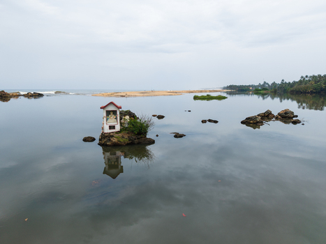 Aerial view of a small Buddhist shrine on a rocky outcrop in calm water with reflections and a sandy beach along the tropical coast Galle Southern Province Sri Lanka. Aerial view of a small Buddhist shrine on a rocky outcrop in calm water with reflections and a sandy beach along the tropical coast Galle Southern Province Sri Lanka.