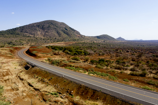 Aerial view of a paved road winding through the arid volcanic landscape of Marsabit with distant hills under a clear blue sky in Marsabit Marsabit County Kenya. Aerial view of a paved road winding through the arid volcanic landscape of Marsabit with distant hills under a clear blue sky in Marsabit Marsabit County Kenya.