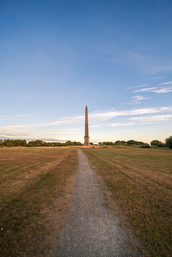 View of the Bodmin Beacon obelisk monument standing at the end of a gravel path in a grassy field under a clear blue sky in Bodmin Cornwall United Kingdom. View of the Bodmin Beacon obelisk monument standing at the end of a gravel path in a grassy field under a clear blue sky in Bodmin Cornwall United Kingdom.