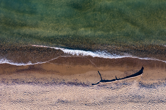 Aerial view of the shore of Lake Michigan with gentle waves washing onto the sandy beach and a piece of driftwood casting a long shadow in Covert Michigan United States.