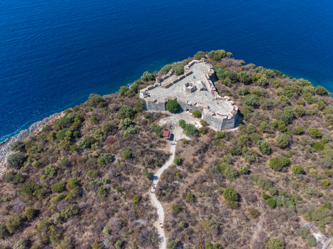 Aerial view of The Castle of Porto Palermo on a rocky peninsula surrounded by the blue Ionian Sea with vegetation and a path leading to the stone fortress in Porto Palermo Qarku i Vlores Albania.
