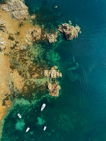 Aerial view of the Paon Lighthouse on the rocky coast of the island of Ile de Brehat with small boats floating in the clear turquoise water Ile de Brehat Brittany France.