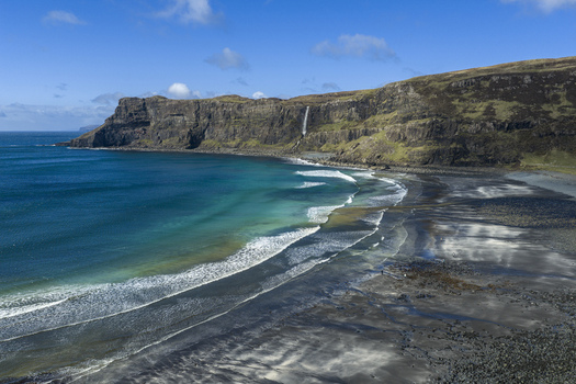 Aerial view of Talisker Bay Beach with its dark sand turquoise water and a waterfall cascading down the rugged cliffs on the Isle of Skye Scotland United Kingdom. Aerial view of Talisker Bay Beach with its dark sand turquoise water and a waterfall cascading down the rugged cliffs on the Isle of Skye Scotland United Kingdom.