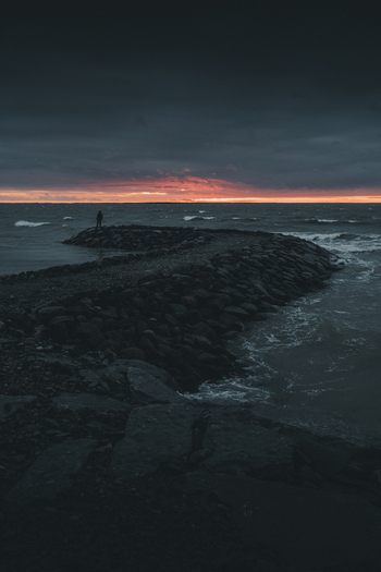View of Saxby rannik with a person standing on the stone breakwater during a dramatic sunset over the sea in Saxby Laane maakond Estonia.