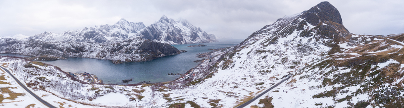 Aerial view of Lofoten featuring snow covered mountains a winding coastal road and a deep blue fjord in the winter landscape of Nordland Norway.