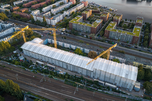 Aerial view of the Schlichtallee residential complex construction site featuring yellow tower cranes extensive white scaffolding and surrounding urban apartment buildings in Berlin Berlin Germany. Aerial view of the Schlichtallee residential complex construction site featuring yellow tower cranes extensive white scaffolding and surrounding urban apartment buildings in Berlin Berlin Germany.