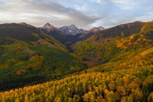 Aerial view of Capitol Peak in the Elk Range with vibrant autumn fall foliage evergreen forests and snow capped peaks under a soft sunrise sky in Snowmass Colorado United States.