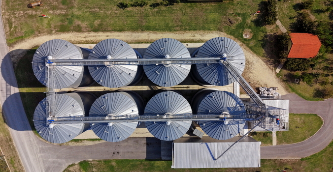 Aerial view of the grain silo complex featuring eight large metal storage bins arranged in a grid with connecting walkways in Bavaniste Vojvodina Serbia.