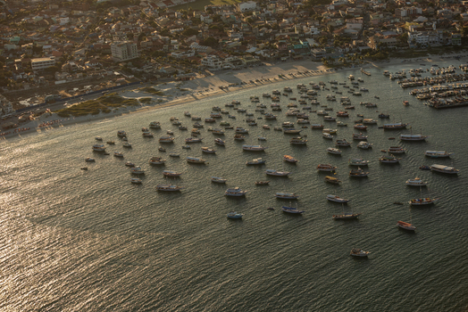 Aerial view of many small boats anchored in a bay near the coastline of Rio de Janeiro with urban buildings visible along the shore at sunset Rio de Janeiro Rio de Janeiro Brazil. Aerial view of many small boats anchored in a bay near the coastline of Rio de Janeiro with urban buildings visible along the shore at sunset Rio de Janeiro Rio de Janeiro Brazil.