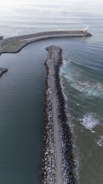 Aerial view of the stone breakwater at Antilla beach with calm waters on one side and waves breaking on the other Gipuzkoa Basque Country Spain.