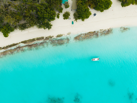 Aerial view of a lone boat cuts through the turquoise waters framed by the white sandy beach and the lush green vegetation of the island Vashafaru Island Thiladhummathi Atoll Maldives. Aerial view of a lone boat cuts through the turquoise waters framed by the white sandy beach and the lush green vegetation of the island Vashafaru Island Thiladhummathi Atoll Maldives.