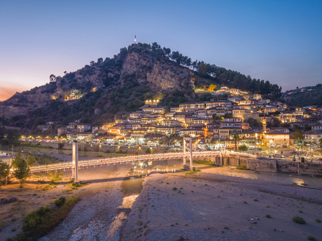 Aerial view of the historic city of Berat with its traditional Ottoman houses the Osum River and a pedestrian bridge illuminated at twilight in Berat Berat County Albania.