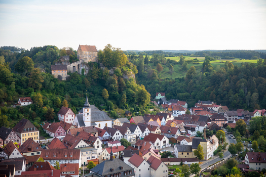 View of Pottenstein Castle overlooking the historic town with its church and traditional red roofed houses nestled in the lush green valley of Franconian Switzerland Pottenstein Bavaria Germany.