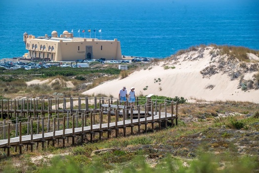 Cascais Lisbon Portugal 19 July 2026 View of the historic Fortaleza do Guincho overlooking sandy dunes and the Atlantic Ocean at Praia do Guincho with a couple on the wooden boardwalk. Cascais Lisbon Portugal 19 July 2026 View of the historic Fortaleza do Guincho overlooking sandy dunes and the Atlantic Ocean at Praia do Guincho with a couple on the wooden boardwalk.