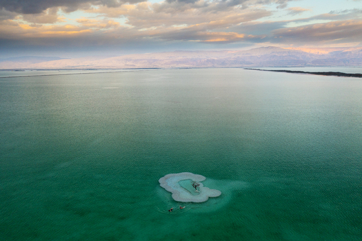 Aerial view of the Dead Sea s turquoise waters embrace a small salt encrusted island under a pastel sky the distant mountains a pale backdrop. Ein Bokek Israel. Aerial view of the Dead Sea s turquoise waters embrace a small salt encrusted island under a pastel sky the distant mountains a pale backdrop. Ein Bokek Israel.