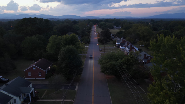 Aerial view of a quiet suburban street at twilight featuring houses trees and a car driving along the road with distant mountains in Lynchburg Virginia United States. Aerial view of a quiet suburban street at twilight featuring houses trees and a car driving along the road with distant mountains in Lynchburg Virginia United States.