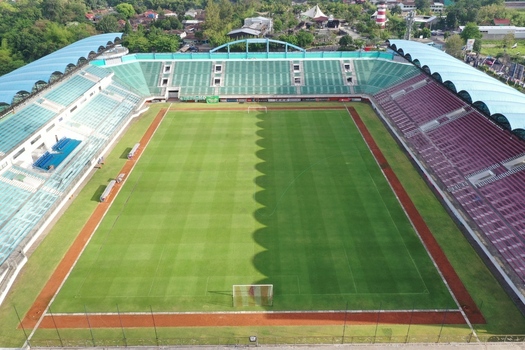 Aerial view of Maguwoharjo Stadium featuring a vibrant green football pitch surrounded by tiered seating and lush trees in Kecamatan Depok Daerah Istimewa Yogya Indonesia.