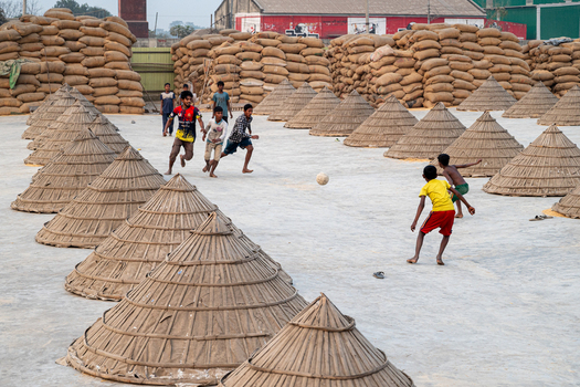 Brahmanbaria Bangladesh 24 January 2026 Aerial view of children playing football in an open yard filled with conical bamboo covers and large stacks of grain sacks.