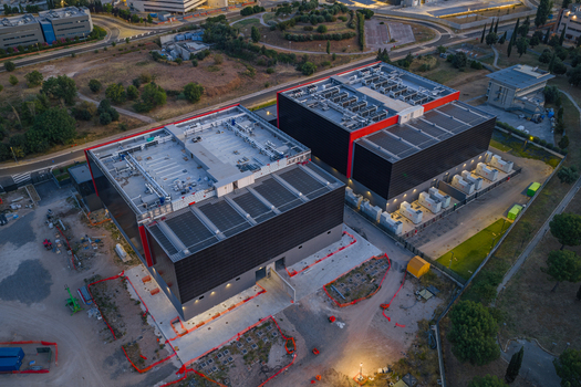 Aerial view of a modern datacenter complex featuring two large industrial buildings with rooftop cooling units and surrounding infrastructure in Settecamini Lazio Italy.