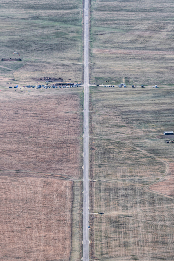 Aerial view of a long straight road stretching through the vast flat plains of the Castelluccio plateau surrounded by agricultural fields in Castelluccio Umbria Italy.