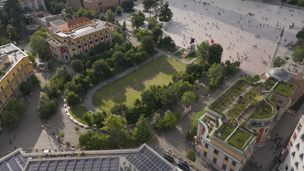 Aerial view of Skanderbeg Square featuring lush green park areas historic architecture the Et hem Bey Mosque and people walking across the expansive plaza in Tirane Tirana County Albania.