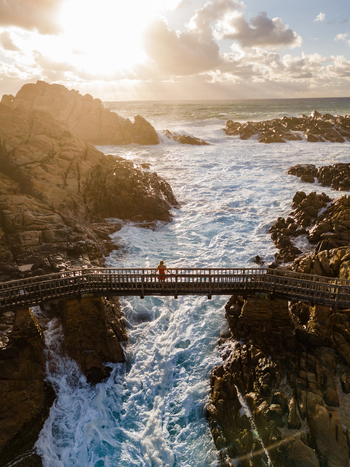 Aerial view of Canal Rocks Bridge with a person standing on the wooden walkway above crashing ocean waves at sunset in Yallingup Western Australia Australia. Aerial view of Canal Rocks Bridge with a person standing on the wooden walkway above crashing ocean waves at sunset in Yallingup Western Australia Australia.