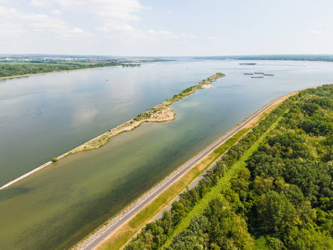 Aerial view of the Danube river with a long sandbar island lush green forest and a coastal road under a bright sky in Bratislava Bratislava Region Slovakia. Aerial view of the Danube river with a long sandbar island lush green forest and a coastal road under a bright sky in Bratislava Bratislava Region Slovakia.
