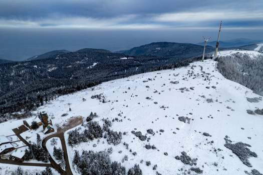 Aerial view of the snow covered Hornisgrinde summit with a wind turbine and communication tower surrounded by pine forests under a cloudy winter sky in Seebach Baden Wurttemberg Germany. Aerial view of the snow covered Hornisgrinde summit with a wind turbine and communication tower surrounded by pine forests under a cloudy winter sky in Seebach Baden Wurttemberg Germany.