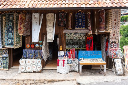 View of a traditional souvenir shop with colorful woven rugs embroidered textiles and local handicrafts displayed on a wooden storefront in Kruje Durres County Albania.