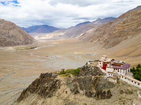 Aerial view of Karsha Monastery perched on a rocky cliff overlooking the vast arid valley and winding road in Zanskar Ladakh India.